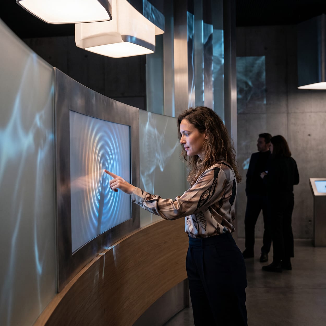 Femeie atingând o suprafață interactivă care reacționează prin lumină și proiecții, ilustrând participarea activă în experiential marketing